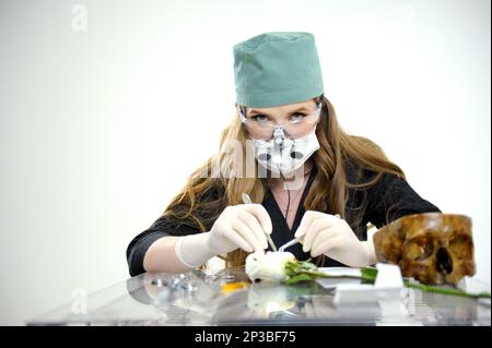 Donna che fa l'ambulatorio che mostra il bisturi dimostrativo e un supporto vicino ad uno spazio vuoto del cranio per il testo guanti chirurgici in lattice vestiti neri tappo verde del medico illuminatore con gli occhiali di sicurezza e binoculare Foto Stock