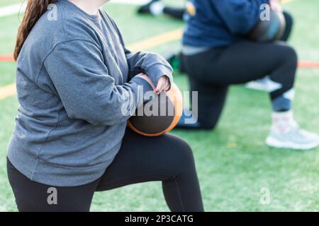 Squadra femminile di tiro e di tiro di campo che riposa su un ginocchio che tiene una palla di medicina durante la pratica. Foto Stock