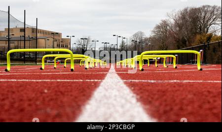 Vista da terra dei mini ostacoli gialli allestiti in corsie su una pista per l'allenamento veloce su una pista di scuola superiore e sul campo. Foto Stock