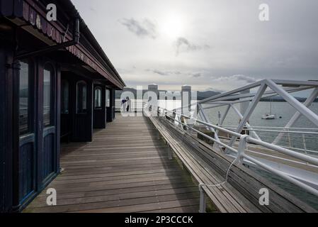 Due uomini che guardano lo stretto di Menai da Beaumaris Pier, Anglesey, Galles del Nord. Foto Stock