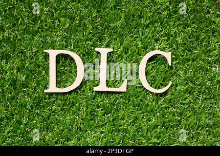 Lettera dell'alfabeto di legno in parola DLC (abbreviazione di contenuto scaricabile) su sfondo verde artificiale Foto Stock