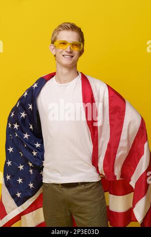 Super American Hero concetto. I giovani sorride in una T-shirt bianca e la bandiera americana è isolata su uno sfondo giallo. Foto di alta qualità Foto Stock