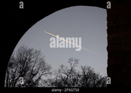 Vista del cielo al tramonto sotto un ponte come un aereo vola in alto lasciando un contrail / percorso vapore / percorso vapore / contraglie nel cielo Foto Stock