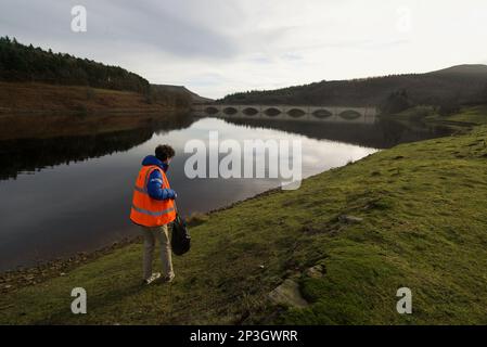 Uomo che raccoglie i rifiuti al Ladybower Reservoir in un giubbotto arancione ad alta visibilità. Foto Stock