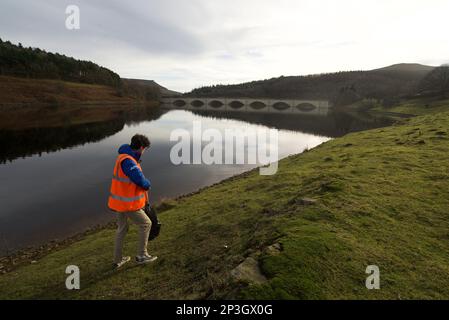 Uomo che raccoglie i rifiuti al Ladybower Reservoir in un giubbotto arancione ad alta visibilità. Foto Stock