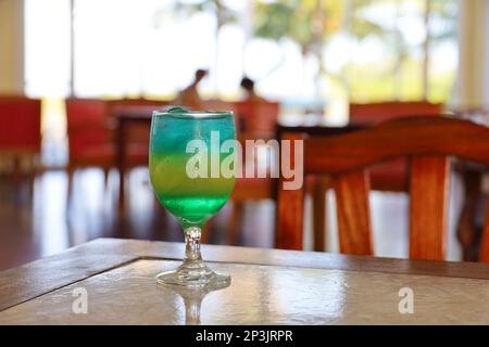 Bicchiere con cocktail fresco su un tavolo su sfondo sfocato coppia. Bar su una spiaggia tropicale Foto Stock