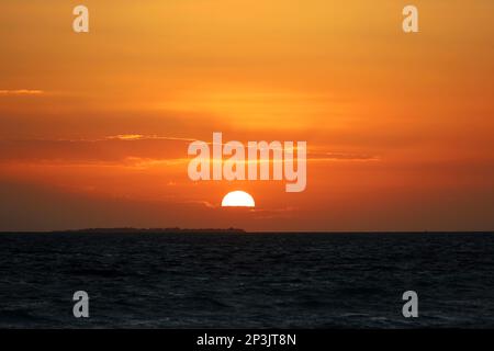 Alba su una spiaggia, il sole arancione splende attraverso le nuvole e si riflette nelle onde scure. Mattina sfondo mare per un viaggio romantico Foto Stock