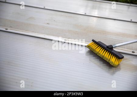 Lavaggio del copricapo pergolato in alluminio. rimuovere le alghe sporche con sapone a spazzola e acqua vicino in giardino da una terrazza casa Foto Stock