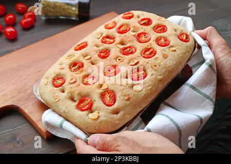 Mettere a mano una padella di pomodoro italiano appena sfornato e focaccia all'aglio su un panino di legno Foto Stock