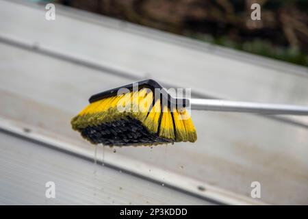 Lavaggio del copricapo pergolato in alluminio. rimuovere le alghe sporche con sapone a spazzola e acqua vicino in giardino da una terrazza casa Foto Stock