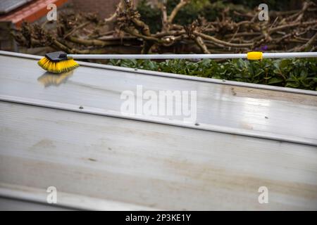 Lavaggio del copricapo pergolato in alluminio. rimuovere le alghe sporche con sapone a spazzola e acqua vicino in giardino da una terrazza casa Foto Stock