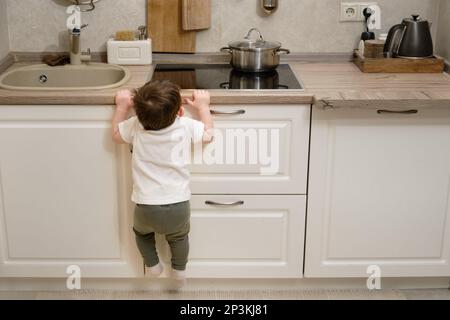 Il bambino salite su una stufa elettrica calda nella cucina domestica. Un bambino piccolo tocca la superficie della stufa con la mano al rischio di ottenere b Foto Stock