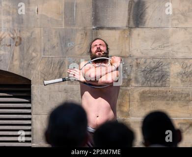 Contorsionista di Street entertainer che si esibisce durante il festival con una racchetta da tennis, Royal Mile, Edimburgo, Scozia, Regno Unito Foto Stock