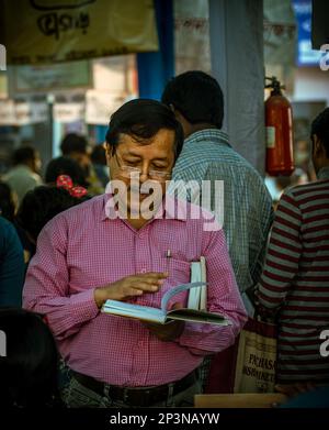 Kolkata, India - 12 febbraio 2023: Un uomo si è ingenuato a leggere un libro in mezzo alla folla vibrante alla Fiera del Libro di Kolkata. Messa a fuoco selettiva. Foto Stock