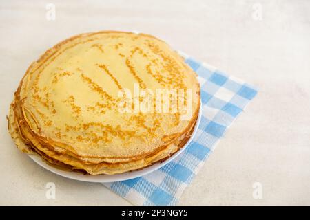 Una pila di frittelle appena sfornate su un tovagliolo blu e bianco sul tavolo. Spazio per il posizionamento delle informazioni. Vista dall'alto. Maslenitsa concerto. Foto Stock