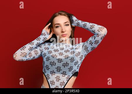 Giovane donna fiduciosa che posa con le mani dietro la testa su sfondo rosso Foto Stock
