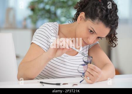 donna che ripara gli occhiali con l'attrezzo in magazzino ottico Foto Stock