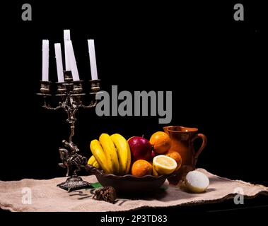 ancora la vita di frutta su un vaso di argilla con un portacandela su uno sfondo scuro Foto Stock
