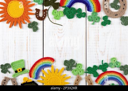 Concetto del giorno di San Patrizio. Composizione a maglia di un cappello verde, un ferro di cavallo, un sole, un arcobaleno e shamrock verde su uno sfondo di legno bianco. Centro di copiatura Foto Stock