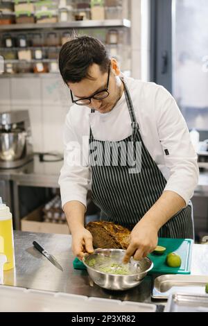 Lo chef sta preparando il cibo. Primo piano di uno chef maschile che prepara toast all'avocado in una spaziosa e moderna cucina. Foto Stock