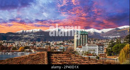 Tramonto a Lugano, montagne innevate e foreste alle spalle. Paesaggio urbano e cornetto in basso a sinistra e foglie autunnali di colore degli alberi in giorno di sole di Begi Foto Stock