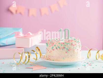 Torta di festa con il numero 10 sullo sfondo del muro rosa festivo con regali e bandiere a serpentina. Foto Stock