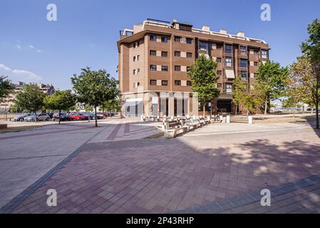 facciata di un nuovo edificio residenziale urbano con alberi giovani accanto ad una grande spianata con panchine in pietra e legno Foto Stock