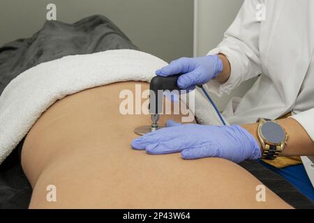 Mani di una massaggiatrice sul dorso di un paziente che applica un massaggio terapeutico con apparecchiature elettriche per trattamenti dermoestetici Foto Stock