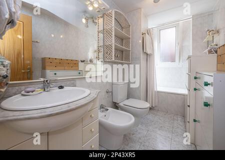 Bagno con lavabo in porcellana bianca su mobile in legno bianco con cassetti e specchio con telaio in legno coordinato Foto Stock