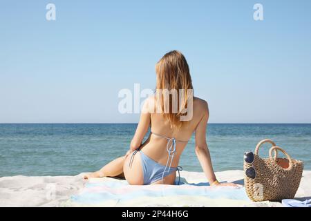 Donna con borsa e altri articoli da spiaggia sulla sabbia vicino al mare, vista sul retro Foto Stock