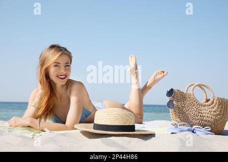 Bella donna con borsa e altri articoli da spiaggia sulla sabbia vicino al mare Foto Stock