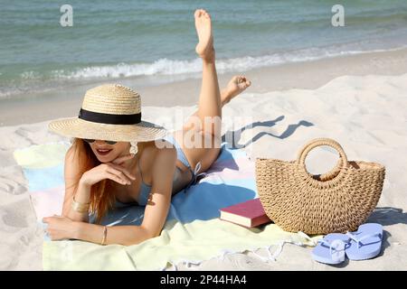 Bella donna con borsa e altri articoli da spiaggia sulla sabbia vicino al mare Foto Stock