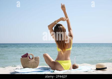 Donna con borsa e altri articoli da spiaggia sulla sabbia vicino al mare, vista sul retro Foto Stock