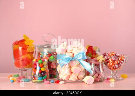 Vasetti con diverse caramelle deliziose su tavola di legno rosa Foto Stock