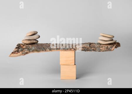 Pile di pietre equilibrate su bastone di legno contro sfondo chiaro. Concetto di armonia Foto Stock