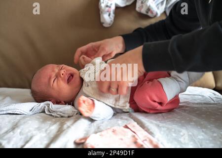 Madre che indossa abiti sulla bambina che piange Foto Stock