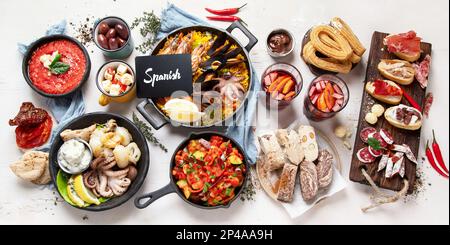 Tipico concetto di tapas spagnole. Il concetto include jamon, salsiccia di chorizo, brushette, ciotola con olive, gamberi, padella con paella, formaggio, sangria, churros Foto Stock