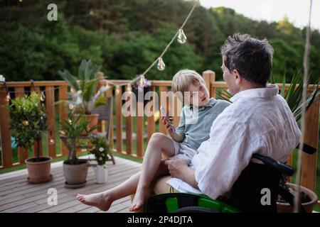 Bambino che mostra il nonno sulla sedia a rotelle qualcosa sul telefono cellulare. Foto Stock