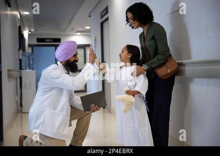 Sikh medico maschile in Turban alto fiorente con figlia e madre abbracciare in ospedale Foto Stock