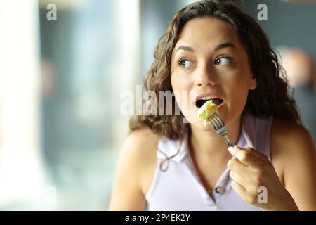 Vista frontale ritratto di una donna che mangia omelette guardando a lato in un ristorante Foto Stock