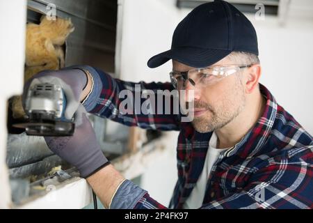 uomo che utilizza una smerigliatrice angolare professionale per il taglio di pareti Foto Stock