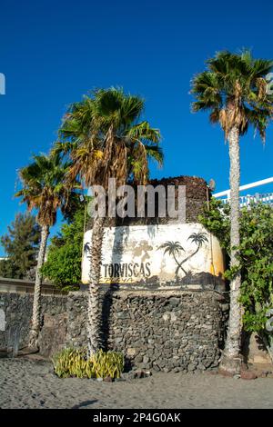 Torviscas Playa scritta su un muro di pietra sulla spiaggia, con palme a Costa Adeje, Tenerife, Spagna Foto Stock