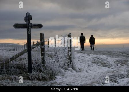 Camminatori sul sentiero coperto di gelo e neve, accanto al cartello e recinzione al tramonto, Ridgeway Path, vicino a Pitstone Hill, Chilterns, Buckinghamshire Foto Stock