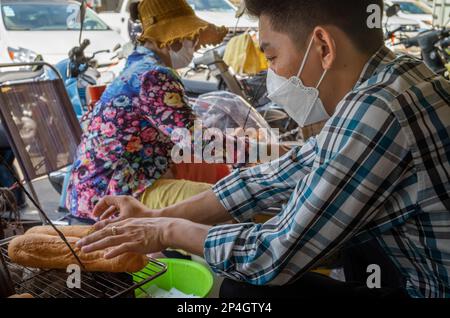 Un uomo riscalda il pane sopra il carbone in una tradizionale paninoteca cambogiana nel mercato centrale, Phnom Penh, Cambogia. Foto Stock