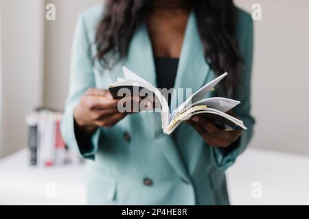 Donna d'affari nera in tuta che flipping attraverso il libro Foto Stock