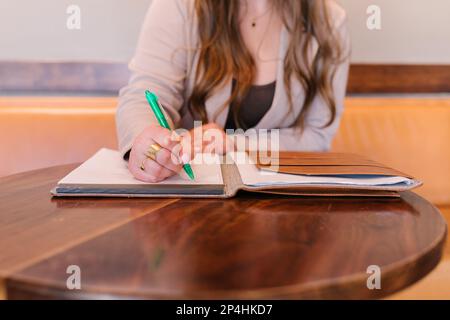 Donna bianca seduta al tavolo circolare marrone scrittura in notebook Foto Stock