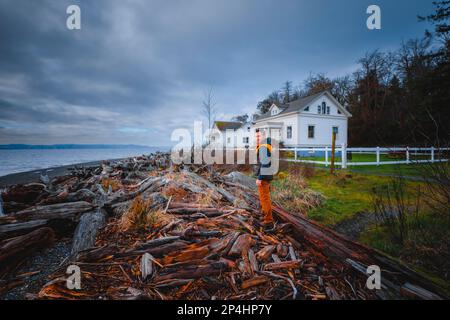 Un uomo è in piedi su tronchi vicino Puget Sound e un edificio storico Foto Stock