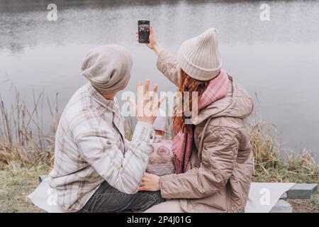 Una famiglia con un bambino piccolo riposa vicino al fiume in tempo freddo Foto Stock
