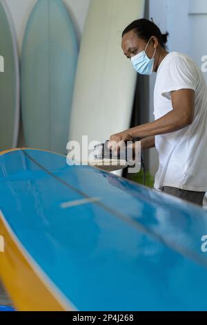 Uomo ripara tavola da surf, mani da vicino, officina di tavola da surf a Bal Foto Stock