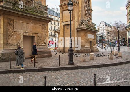 Un uomo si gira per guardare una donna che passa sotto la Porte Saint-Denis a Parigi. Foto Stock